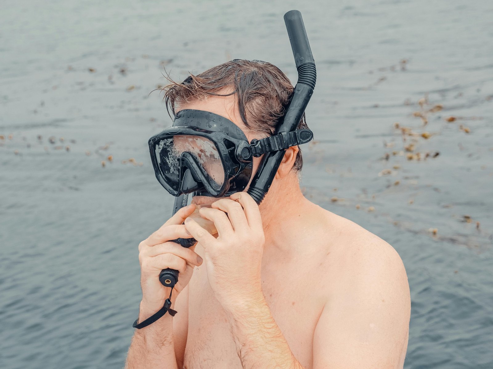 Person adjusting a snorkel mask at the water's surface.